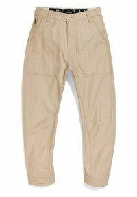 Krémové volné kalhoty s předními náprsními kapsami, zapínáním na knoflík, poutky na pásek a viditelnými stehy podél švů a kolen.