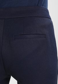 Marinblå byxor i bomullsblandning med en strukturerad yta, utrustade med en bakficka och en platt midja.