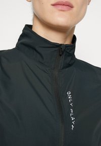 Black windbreaker jacket featuring a high collar, front zipper, and left chest text in white: "ONLY PLAY." Lightweight, smooth texture.