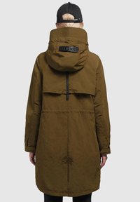 Olivově zelený dlouhý parka kabát s kapucí, vybavený zipovým zapínáním, skládacími detaily na zádech a velkým logem na zádech. Hladká, texturovaná látka.