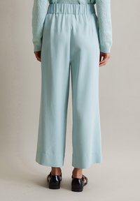 Vaaleansiniset, leveälahkeiset housut pehmeällä ja sileällä pinnalla sekä joustavalla vyötäröllä, joiden helma ulottuu juuri nilkan ylle.