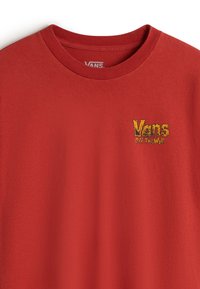 T-shirt Vans rouge col rond avec petit logo jaune "Vans Off The Wall" sur la partie gauche de la poitrine.