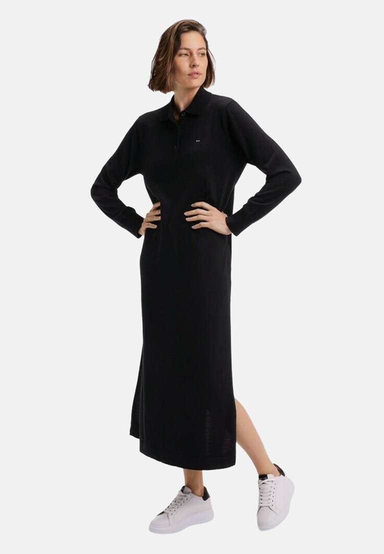Robe polo noire à manches longues avec un col, texture côtelée, fentes latérales et coupe décontractée, associée à des baskets blanches avec des accents noirs.