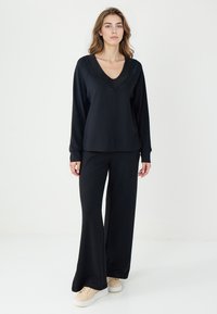 Czarny zestaw odzieży wypoczynkowej składający się z długiego rękawa topu w dekoltem w kształcie V oraz szerokich spodni, oba wykonane z gładkiego, miękkiego materiału. Zdobiony żebrowanym dekoltem.