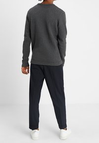 Pull en maille grise avec un motif texturé, col rond et manches longues, associé à un pantalon bleu marine fuselé et des baskets blanches.