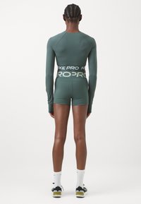Hosszú ujjú, türkiz színű sportfelső fekete "NIKE PRO" derékkal, passzoló sorttal párosítva. Simább textúrával és testhez simuló kialakítással.