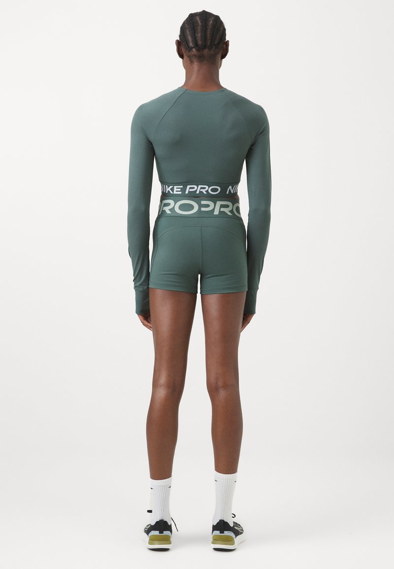 Haut de sport à manches longues en bleu sarcelle avec une ceinture noire "NIKE PRO", accompagné de short assortis. Texture lisse avec un design ajusté.