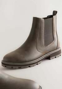 Brun läder Chelsea-boot med elastisk sidopanel, dragflik och tjock räfflad sula på en ljus bakgrund.