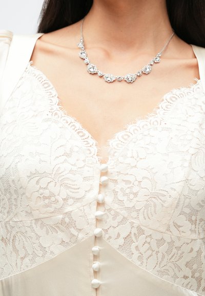 Nėriniuota kremine bodis su gėlių raštais ir sagų detalėmis, derančiais su sidabrine vėriniu, puoštą gėlių akcentais ir cirkoniais.