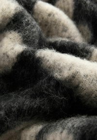 Villasekoituskangas, jossa on pehmeä, teksturoitu pinta ja musta-kreemivärinen kuvio, joka esittelee kiinteiden ja laikukkaiden värien sekoitusta.