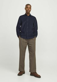 Camicia blu navy con maniche lunghe, abbinata a pantaloni marroni chiari. La camicia ha un colletto classico e una texture sottile. Le scarpe marroni completano il look.
