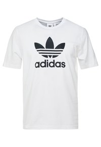 Bílá bavlněná tričko s černým logem Adidas a třemi pruhy a grafikou trojlístku na přední straně. Krátké rukávy, design s kulatým výstřihem.