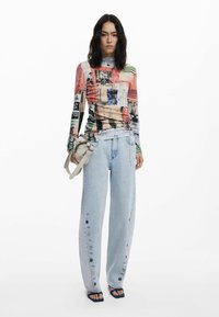 Langarm, mehrfarbiges Grafikt-Shirt kombiniert mit hellblauen weit geschnittenen Jeans mit dekorativen Knöpfen und einer Umhängetasche.