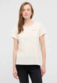 Krēmkrāsas īso piedurkņu T-krekls, izgatavots no mīksta kokvilnas materiāla. Tam ir apaļa kakla izgriezuma forma un neliels sarkans "MUSTANG" logo uz krūšu daļas.