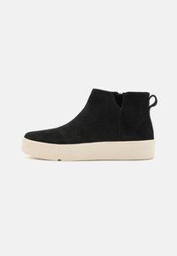 Juodos suede kulkšnies botai turi pakeltą smėlio spalvos padas, apvalų pirštą, šoninius užtrauktukus ir mažą užsegimą gale, kad būtų lengviau apsiauti.