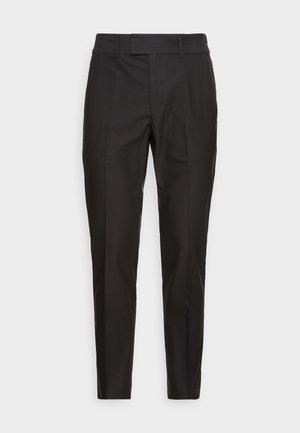 Zwarte, op maat gemaakte slim-fit broek met lussen voor een riem en geplooide vouwen, afgebeeld tegen een effen lichte achtergrond.