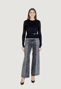 Haut noir à rayures et à manches longues associé à un jean en denim gris à jambes larges avec un design fendu. Le mannequin porte des talons noirs et se tient devant un fond neutre.