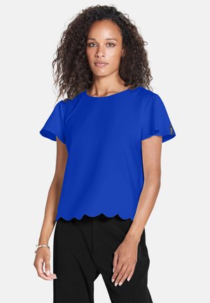 Blusa corta blu royal con maniche a sbuffo e orlo scallop. Realizzata in tessuto morbido; dettagli includono sottili elementi del marchio.