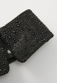 Must have mustekott, mis on valmistatud tekstureeritud materjalist, kaunistatud erinevas suuruses mustade rhinestone'idega, varustatud lukuga ja diskreetse logo detailiga.