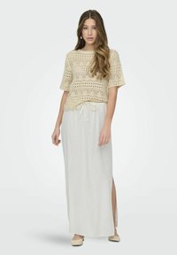 Top de punto beige con mangas cortas y patrón calado, combinado con una falda maxi blanca con cintura ajustable y abertura lateral.