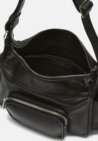 Sac à main en cuir noir avec un compartiment principal zippé, texture lisse, poche zippée extérieure et une bandoulière réglable.
