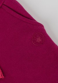 Fuchsia Pullover mit strukturiertem Strick, ausgestattet mit einem runden Logo-Patch in einer etwas dunkleren Nuance. Glattes Material mit einer weichen Oberflächenbeschaffenheit.