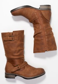 Hnědé kožené ankle boty s volným designem, bočním zipem a dekorativním páskem se zapleteným akcentem. Černá gumová podrážka.