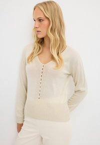 Beige gebreide trui met een V-hals en lange mouwen, voorzien van een knoopsluiting aan de voorkant en ribbeltextuur aan de zoom.