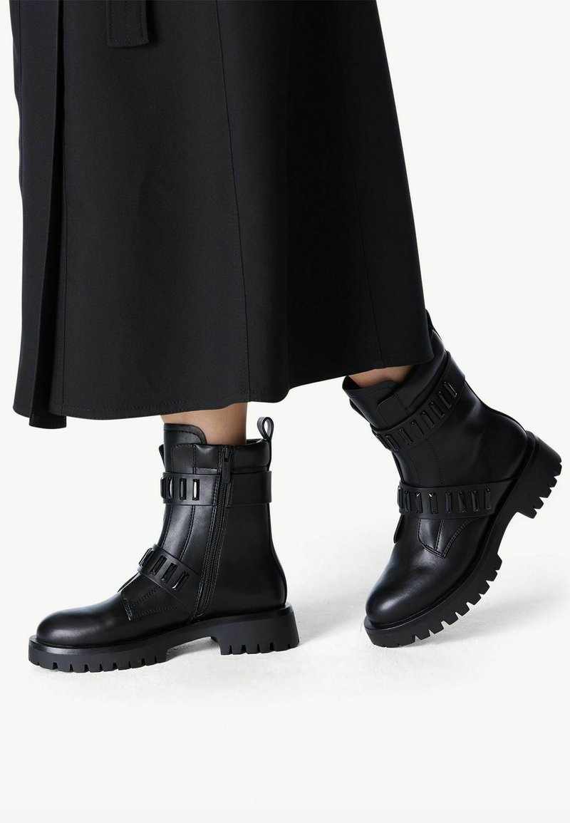 Black leather combat boots with a rubber sole, featuring a side zipper, strap accents, and a textured upper with a sturdy design.