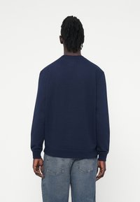 Felpa blu navy con scollatura a girocollo e polsini a costine. Tessuto morbido con una texture liscia, caratterizzata da un design semplice e da dettagli di cucitura discreti.