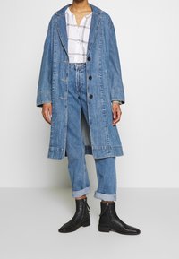 Denimjacka i ljusblå färg, oversized passform, enfärgad design, stor krage och svarta knappar; matchad med uppvikta denimbyxor och svarta ankelstövlar.