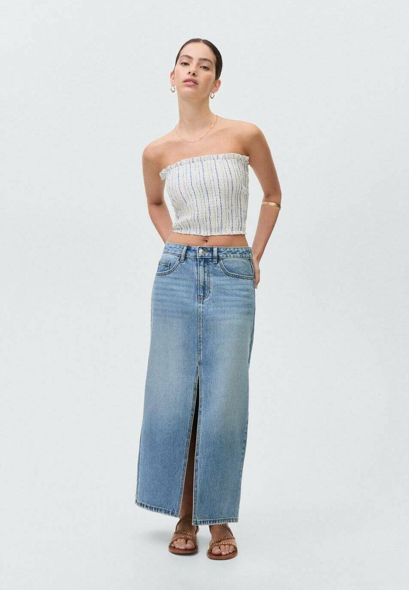 Top brez naramnic v beli barvi z modrimi črtami; svetlo modra visokoproga denim krila z razporkom spredaj; rjave sandale s trakci; gladka tekstura.