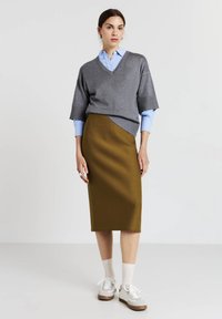 Maglione grigio a maniche corte con scollatura a V indossato sopra una camicia azzurro chiaro, abbinato a una gonna a matita verde oliva lunghezza ginocchio e sneakers bianche.