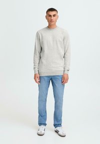 Grå hettegenser med rund hals, lange ermer og ribbestrikkede mansjetter, kombinert med lyseblå jeans og svart-hvite joggesko. Enkel design.