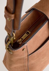 Sac à main en daim marron avec zip doré et fermoir en métal, couture détaillée, et bandoulière ajustable, vue en gros plan.