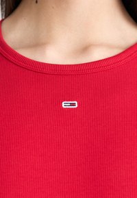 Camiseta roja de canalé con cuello redondo. Presenta un pequeño logotipo bordado en blanco, azul y rojo en la zona del pecho.