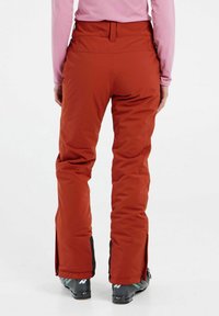 Pantaloni da neve da donna in arancione, con una vestibilità affusolata, vita regolabile, ventilazione con cerniera alle gambe e dettagli neri ai polsini.