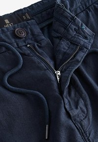 Navy blue pants with a textured fabric, featuring a front zipper, a button closure, and drawstring at the waist.