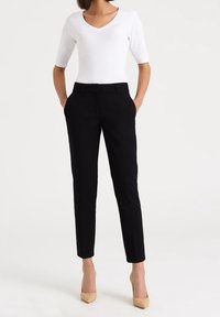 Pantalon noir sur mesure à coupe droite avec poches latérales, associé à un haut blanc à col en V. Le mannequin porte des talons hauts beiges. Texture du tissu lisse.