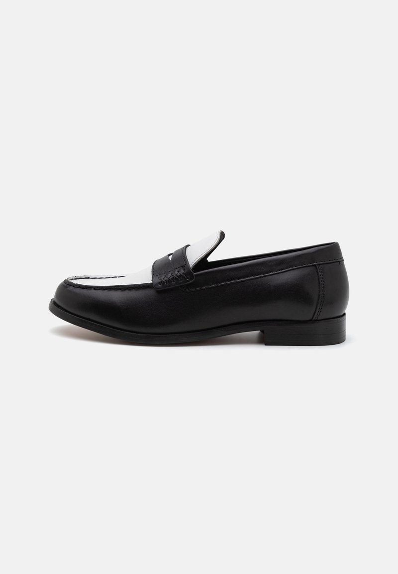 Mocassin en cuir noir et blanc avec bout moc cousu et bride à monnaie, présenté de côté sur un fond blanc uni.