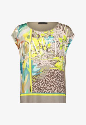 Chemise beige à manches courtes avec des motifs floraux colorés et imprimés léopard, et le mot "WOMEN" en travers sur le devant dans une police stylisée.