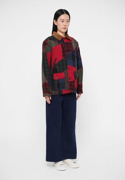 Μπουφάν πατςγουορκ με καρό σχέδια σε κόκκινο, πράσινο και μπλε, με καφέ γιακά, δύο μπροστινές τσέπες και κουμπώματα με κουμπιά. Συνδυάζεται με μπλε σκούρο παντελόνι.