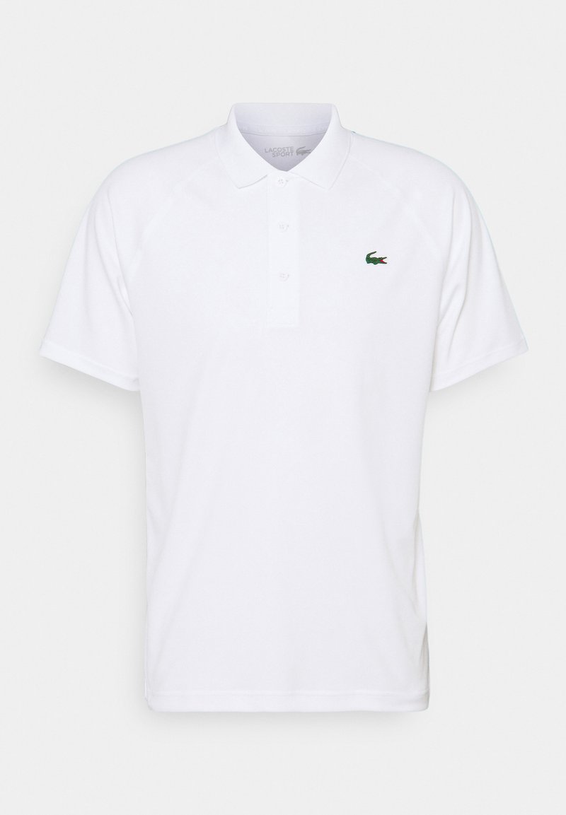 Vit polo skjorta med klassisk krage, placket med tre knappar och grön Lacoste krokodil-logotyp på bröstet. Korta raglanärmar.