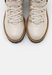 Bottines en cuir beige clair avec quincaillerie dorée, présentant une tige texturée, des lacets tissés et une semelle en caoutchouc noir robuste.