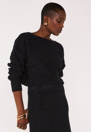Pull en maille noire avec un col large et une coupe ample, agrémenté de légers accents scintillants, assorti à une jupe de texture similaire.