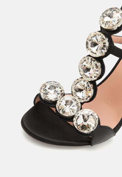 Melnas satīna sandales ar lieliem caurspīdīgiem rhinestones, atvērta purngalu un izliekta forma. Iezīmējas ar gludu tekstūru un mīkstu rozā iekšzoli.