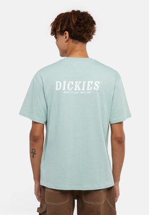 Camiseta de algodón azul claro con texto de logo blanco en la parte posterior, manga corta y corte relajado. Diseño simple, sin patrones ni acentos.