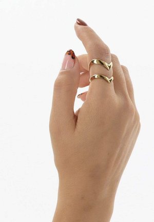 Main avec un teint beige portant deux bagues dorées ondulées à l'annulaire et des ongles peints avec un motif léopard beige et noir.