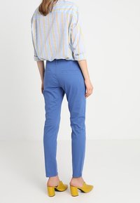 Světle modrá pruhovaná košile spárovaná s modrými slim-fit kalhotami. Žluté podpatkové muly dotváří vzhled. Jasný, propracovaný silueta a živé barvy.