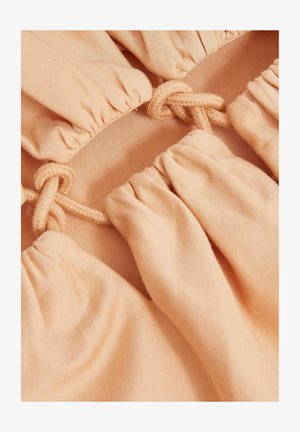 Őszibarack színű szövet, meggyűrt részekkel. Középen díszes, csomózott zsinór részlet található, amely texturált, redőzött hatást kelt.